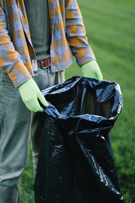 Two large black plastic rubbish bags, filled and tied, are positioned on the edge of a paved sidewalk near a curb. The bags are visibly crumpled and appear to contain household waste or discarded mate